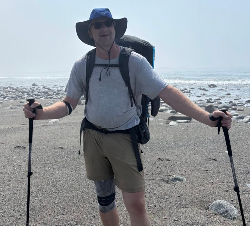 Jason Van Bergen wearing a heavy backpack and knee brace on the beach during the West Coast Trail.